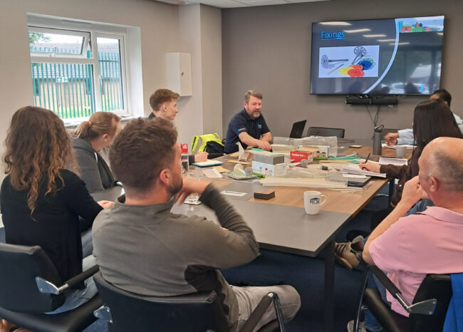A group on Benx employees around a boardroom table listening to a trainer explain EWI fixings